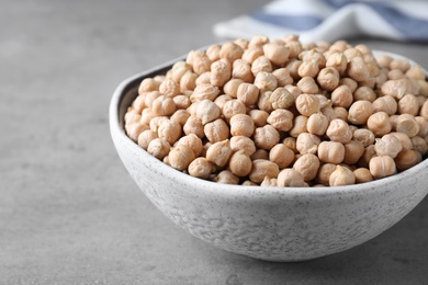 Photo of Raw chickpeas in bowl on grey table, closeup