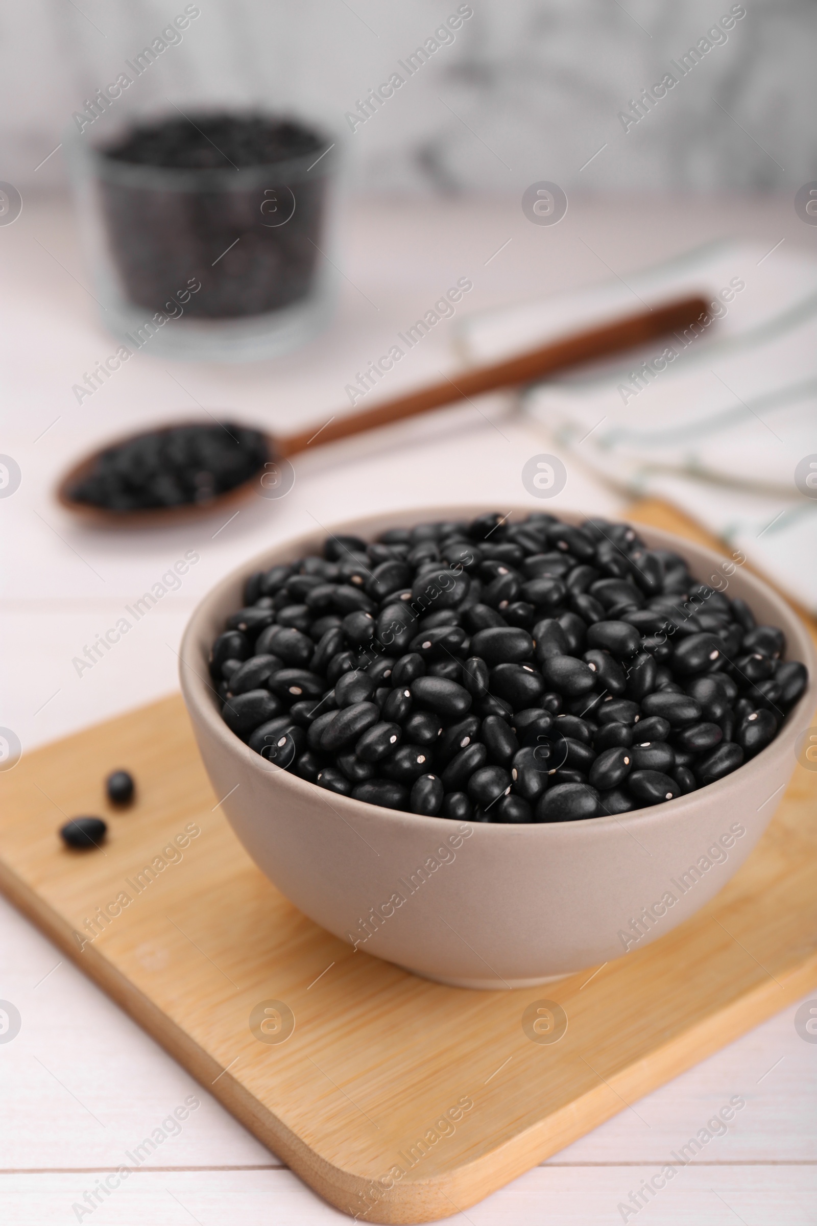 Photo of Bowl of raw black beans on white wooden table, closeup