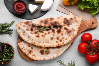 Photo of Delicious calzones and products on grey table, flat lay