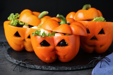 Photo of Bell peppers with black olives, mozzarella and lettuce as Halloween monsters on dark table, closeup