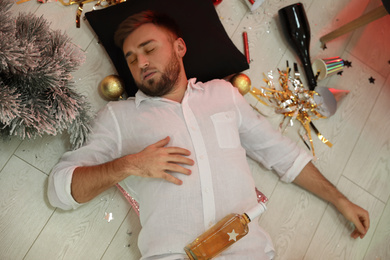 Photo of Drunk man sleeping on floor in messy room after New Year party, above view