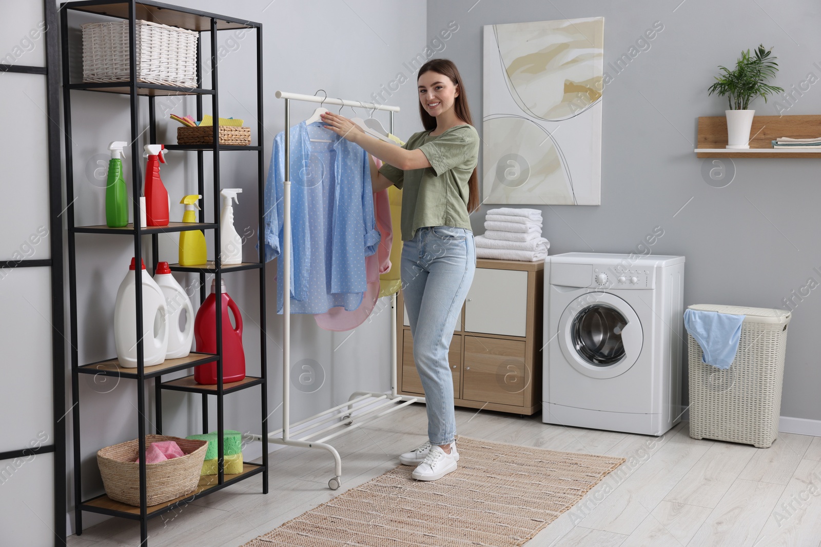 Photo of Young woman taking shirt from rack in laundry room