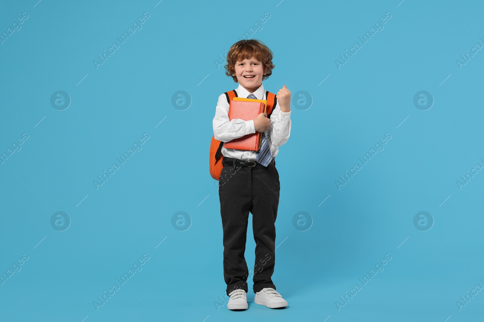 Photo of Happy schoolboy with backpack and books on light blue background