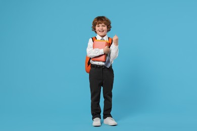 Photo of Happy schoolboy with backpack and books on light blue background