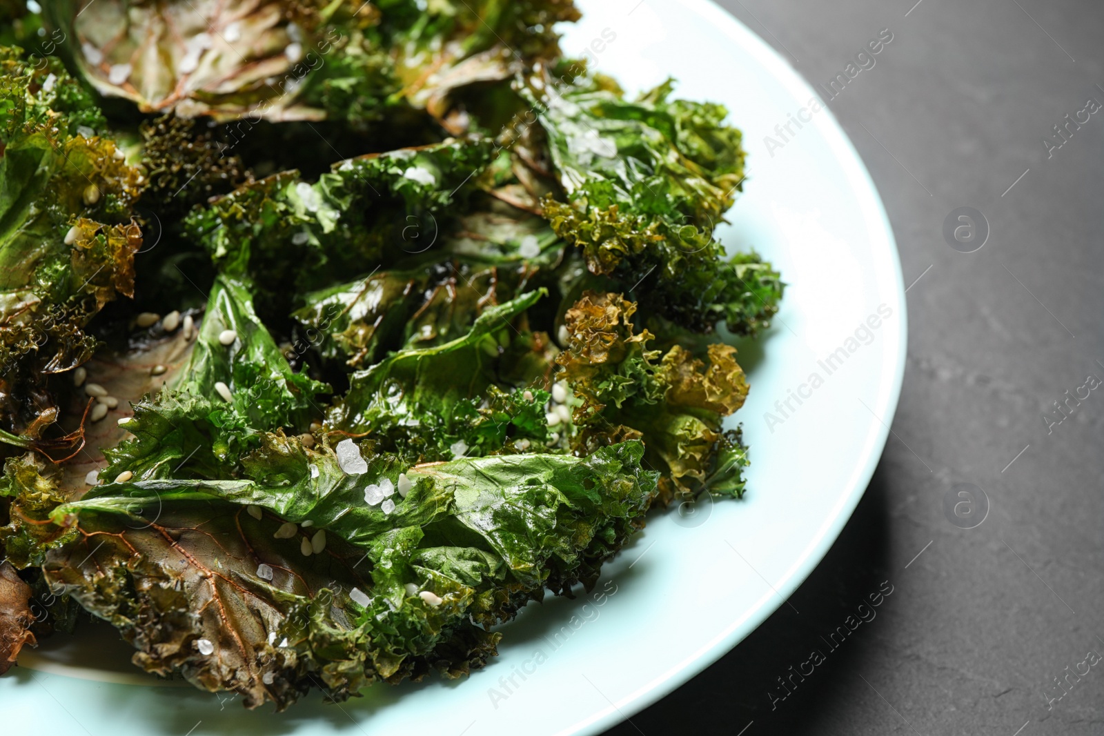 Photo of Tasty baked kale chips on dark grey table, closeup