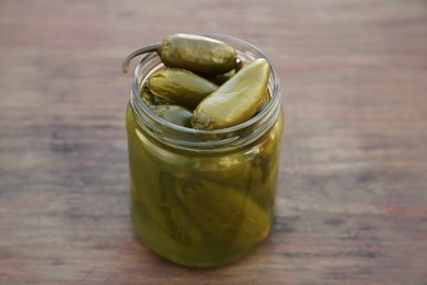 Photo of Glass jar of pickled green jalapeno peppers on wooden table, closeup