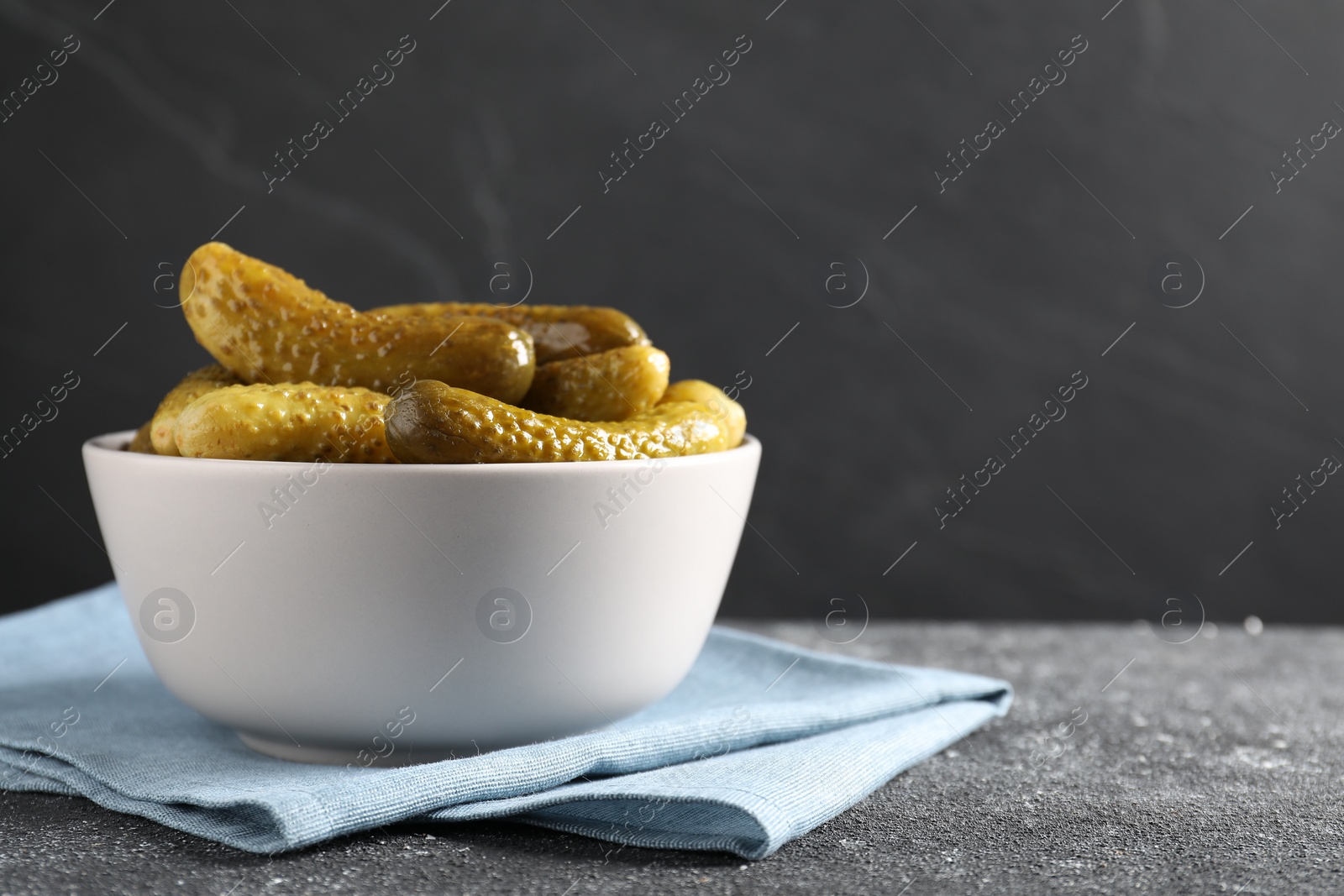 Photo of Tasty pickled cucumbers in bowl on grey textured table, space for text