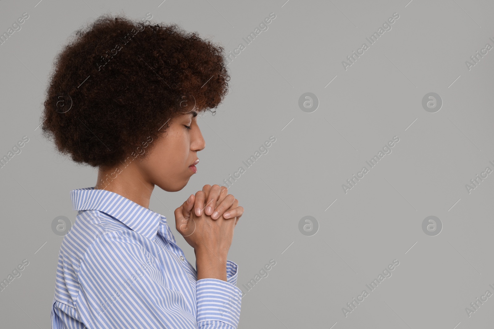 Photo of Woman with clasped hands praying to God on grey background. Space for text