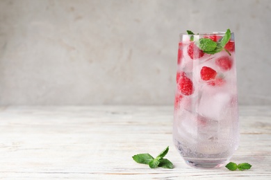 Glass of refreshing drink with raspberry and mint on light wooden table against grey background, space for text