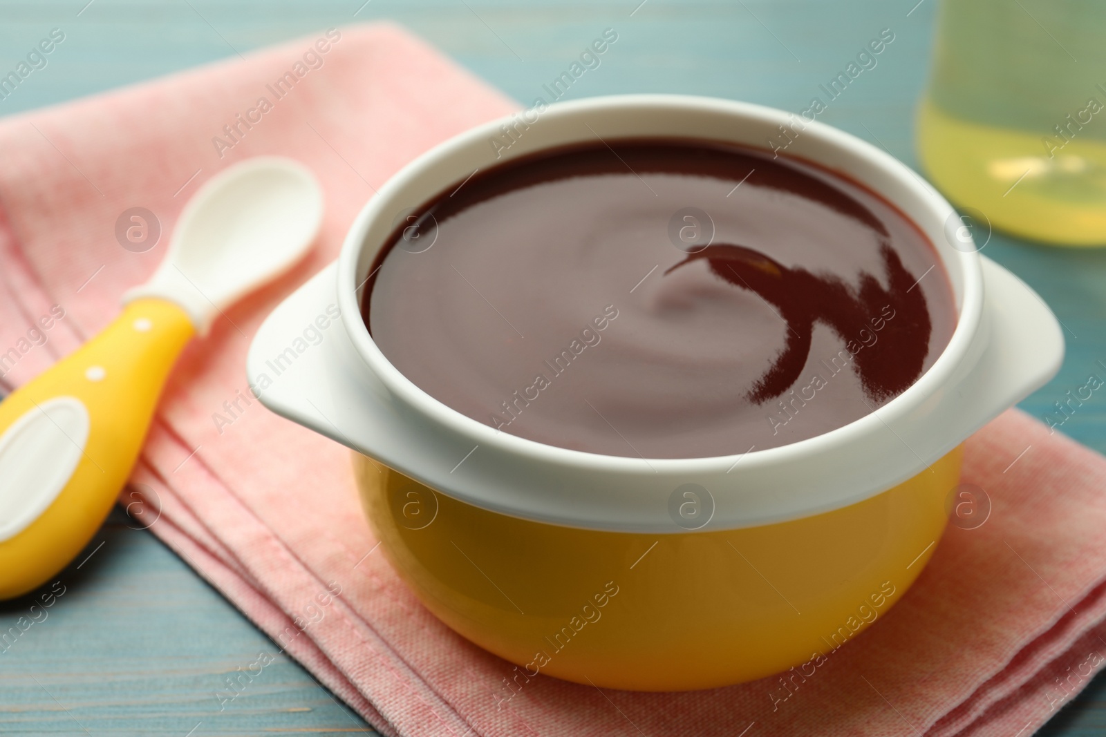 Photo of Bowl with tasty pureed baby food on light blue wooden table, closeup