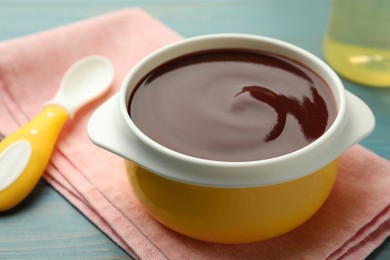 Photo of Bowl with tasty pureed baby food on light blue wooden table, closeup