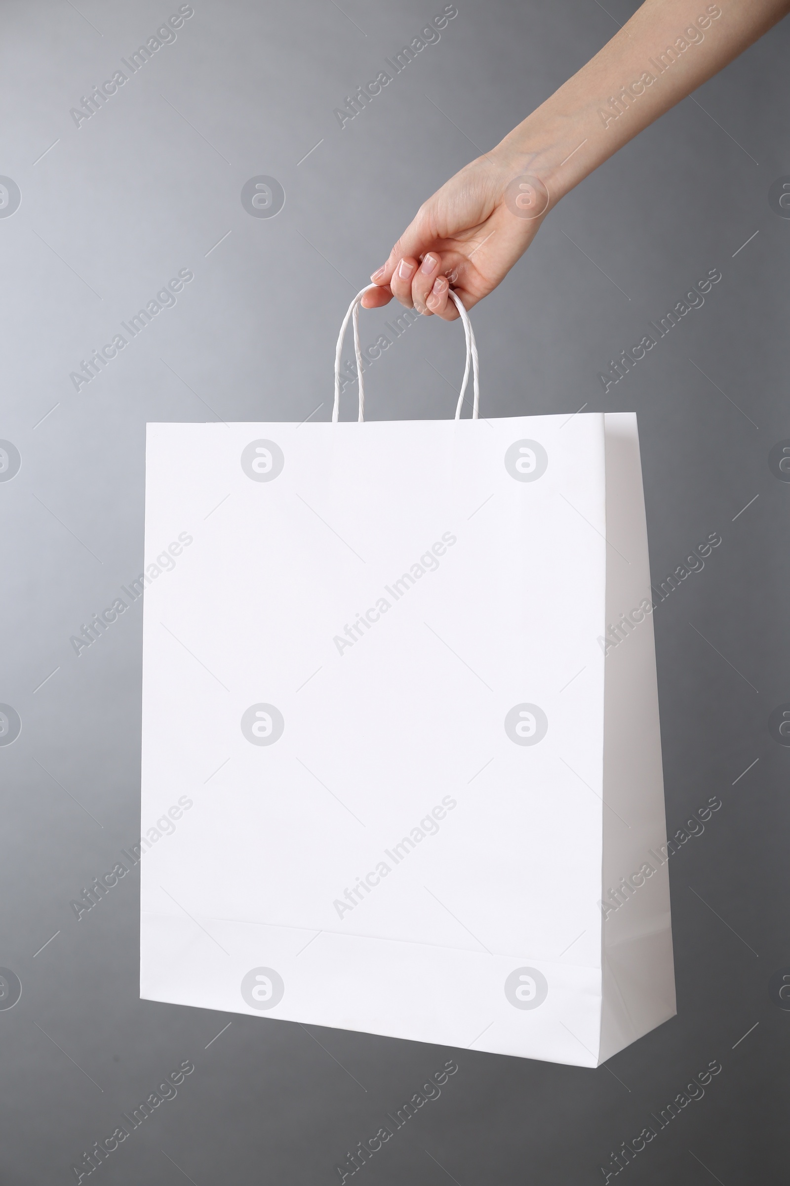 Photo of Woman holding white paper bag on grey background, closeup. Mockup for design