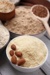 Bowls with different types of flour and ingredients on white wooden table, closeup