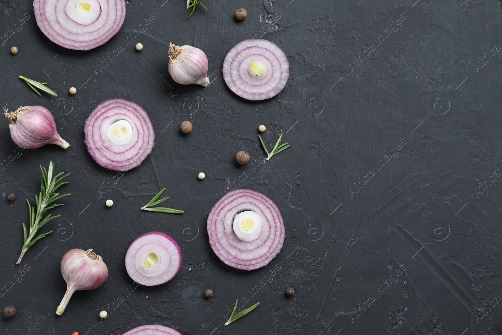 Photo of Fresh raw garlic heads, onion rings and spices on black table, flat lay. Space for text