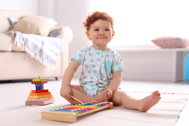Photo of Cute little child playing with xylophone on floor at home