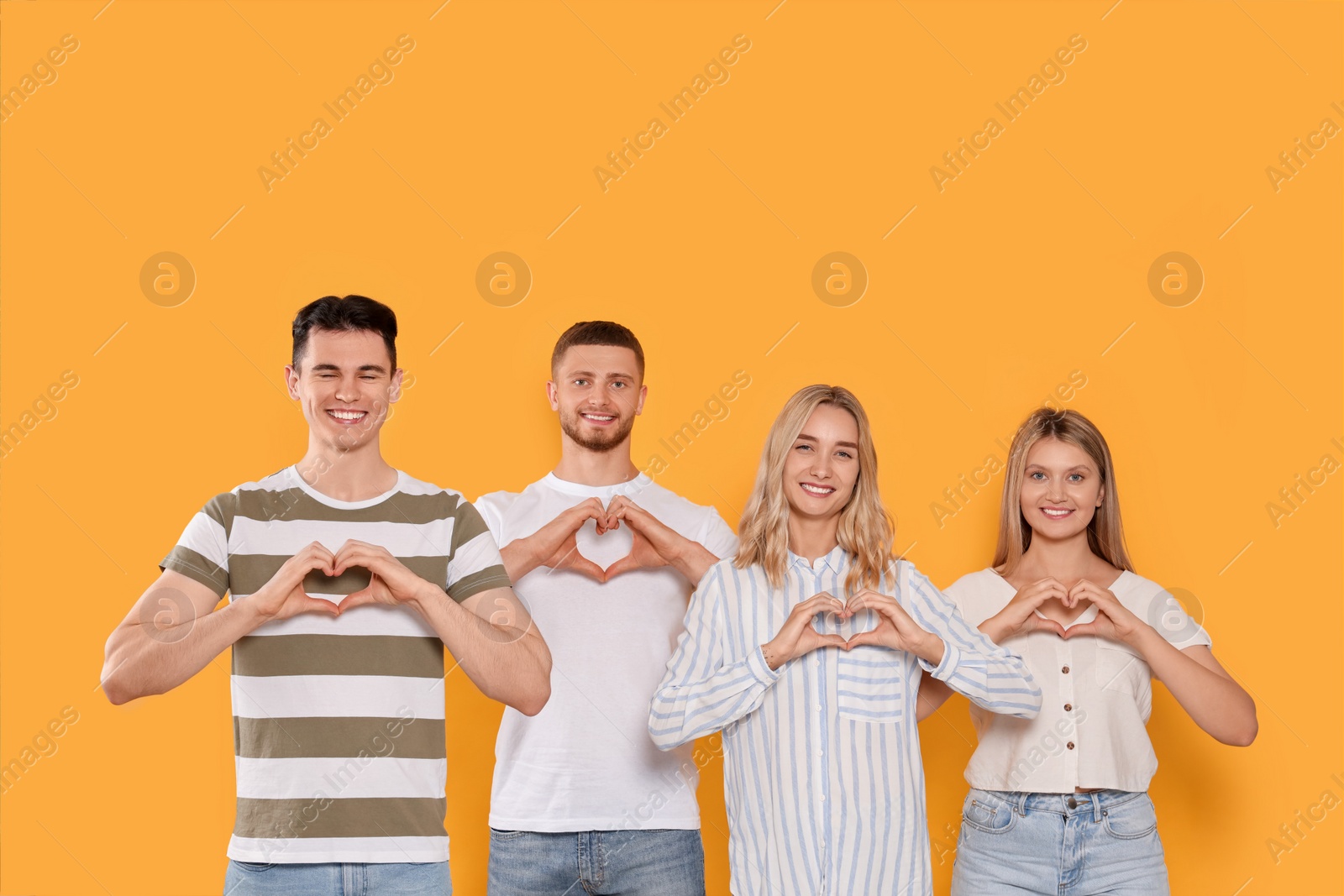 Photo of Happy volunteers making hearts with their hands on orange background