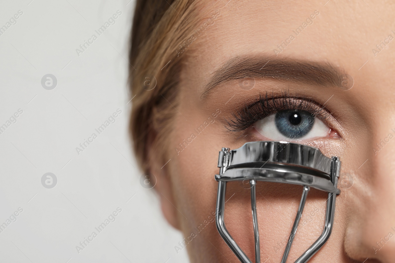 Photo of Young woman using eyelash curler on white background, closeup. Space for text