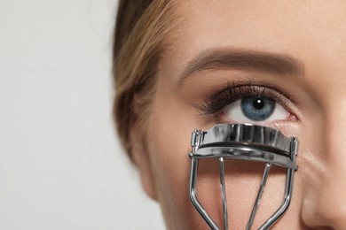 Young woman using eyelash curler on white background, closeup. Space for text