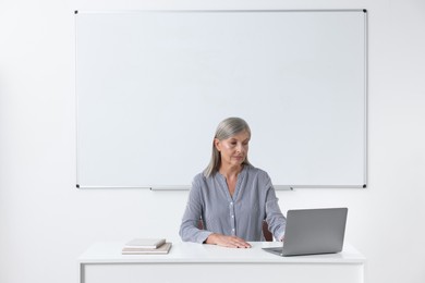 Photo of Professor sitting near laptop at desk in classroom