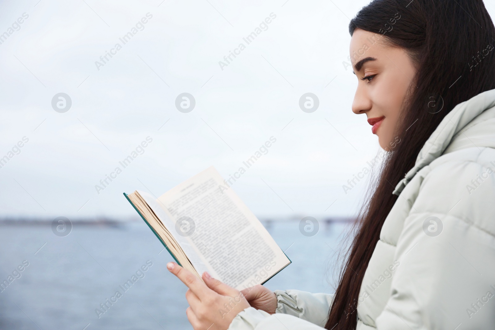 Photo of Woman reading book near river on cloudy day