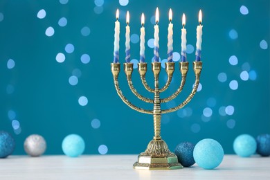 Hanukkah celebration. Menorah with burning candles and baubles on table against blue background with blurred lights, space for text