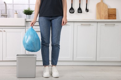 Photo of Woman taking garbage bag out of trash bin in kitchen, closeup. Space for text