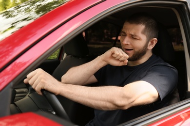 Tired man yawning while driving his modern car