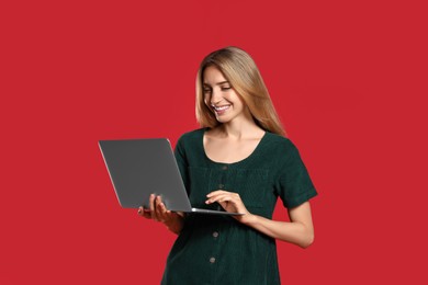 Portrait of young woman with modern laptop on red background