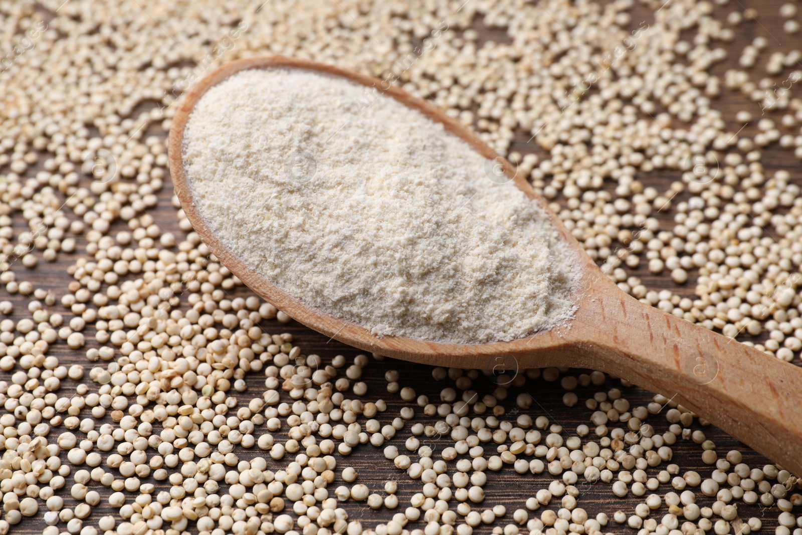 Photo of Spoon with quinoa flour and seeds on wooden table, closeup