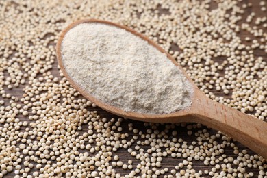 Spoon with quinoa flour and seeds on wooden table, closeup