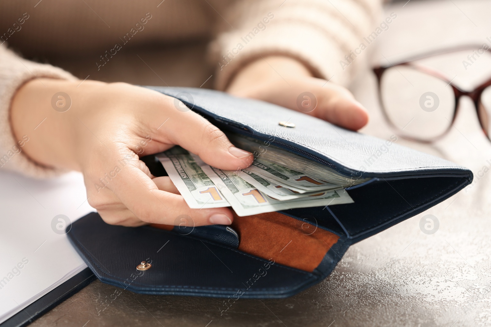 Photo of Woman putting money into wallet at brown table, closeup