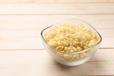 Photo of Delicious bulgur in glass bowl on wooden table, closeup. Space for text