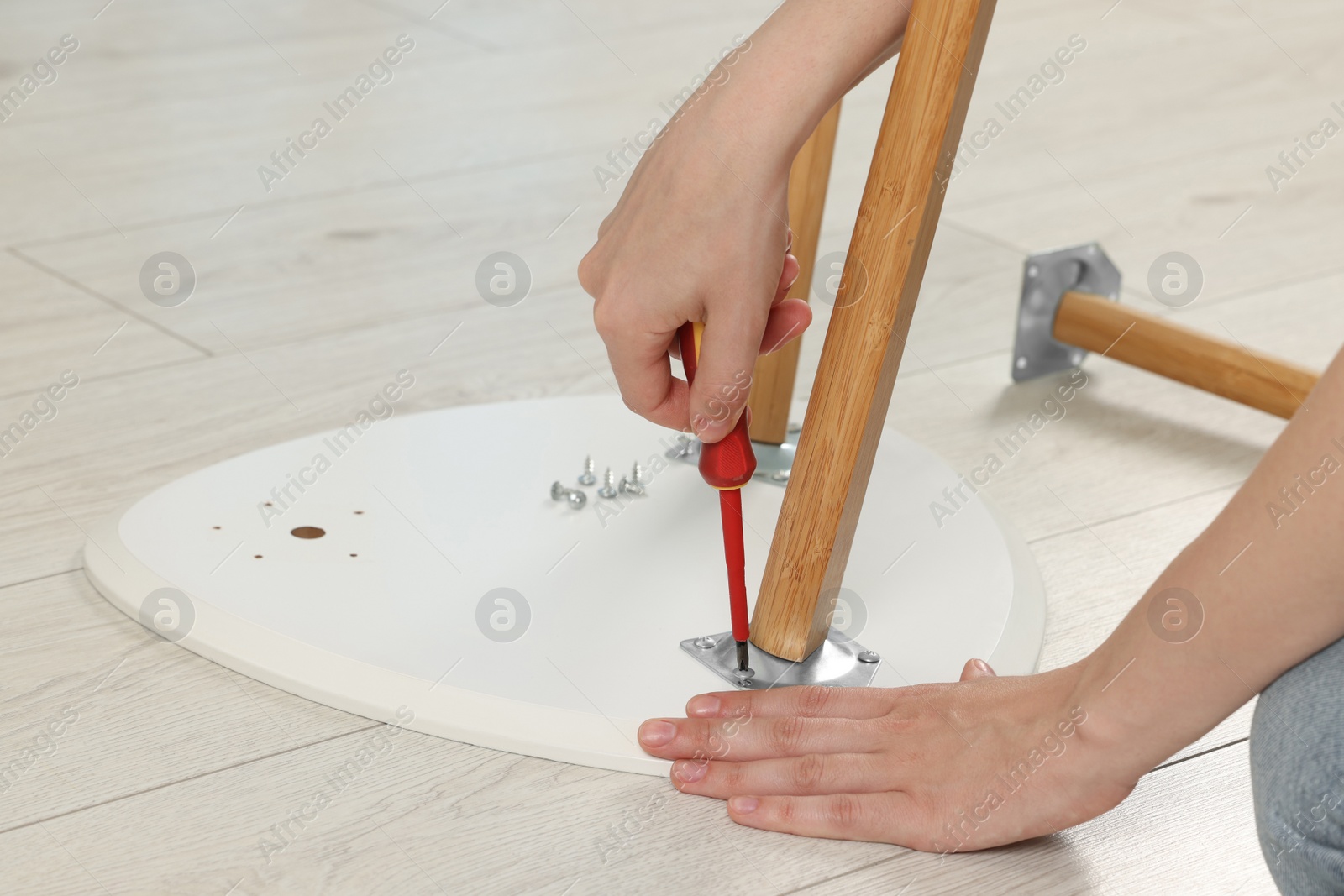 Photo of Woman with screwdriver assembling stool on floor, closeup