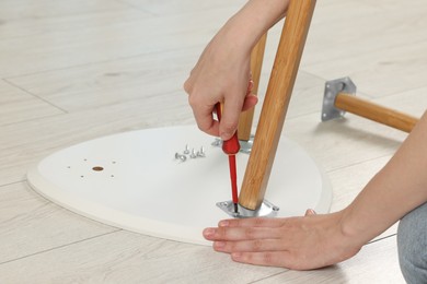 Photo of Woman with screwdriver assembling stool on floor, closeup