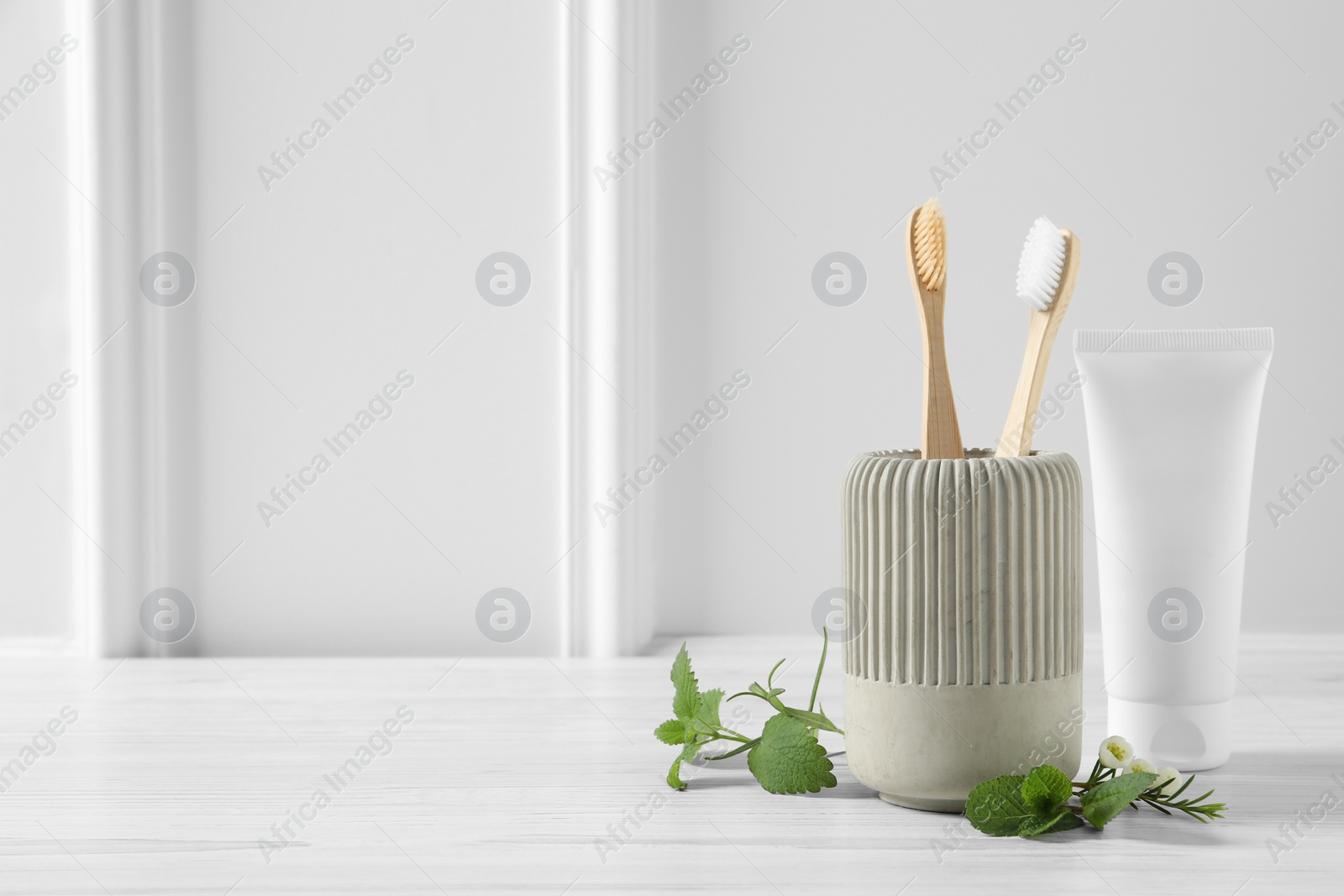 Photo of Toothbrushes, toothpaste and herbs on white wooden table. Space for text