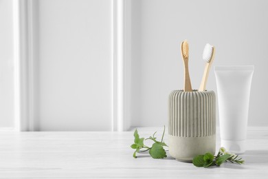 Toothbrushes, toothpaste and herbs on white wooden table. Space for text