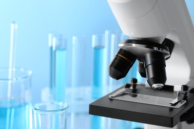 Microscope and test tubes with light blue liquid in laboratory, closeup. Space for text