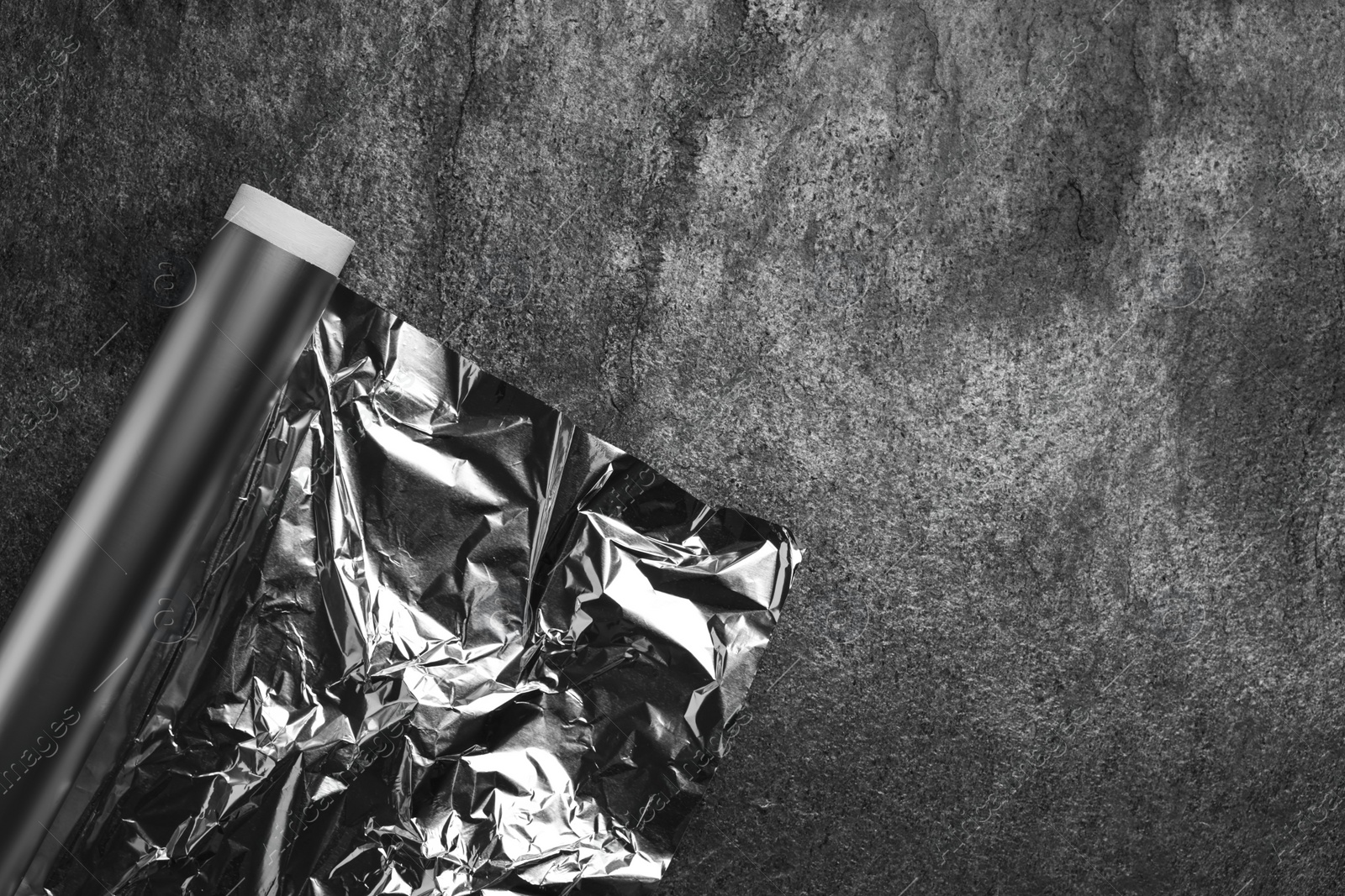 Photo of Roll of aluminum foil on grey table, top view. Space for text