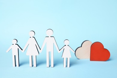 Photo of Figures of family stainding near heart on light blue background. Insurance concept