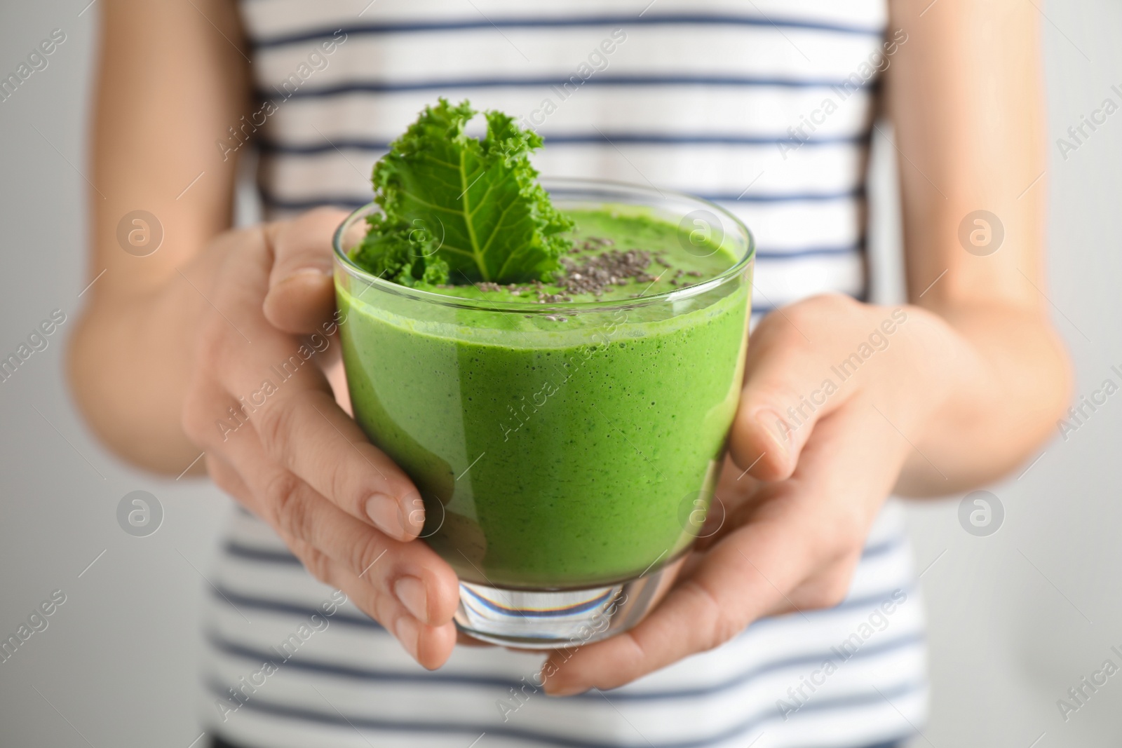 Photo of Woman holding tasty kale smoothie with chia seeds on light background, closeup