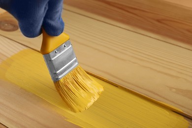 Photo of Worker applying yellow paint onto wooden surface, closeup. Space for text