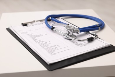 Photo of Clipboard and stethoscope on white table in clinic, closeup. Doctor's workplace