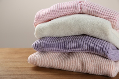 Stack of knitted sweaters on wooden table, closeup