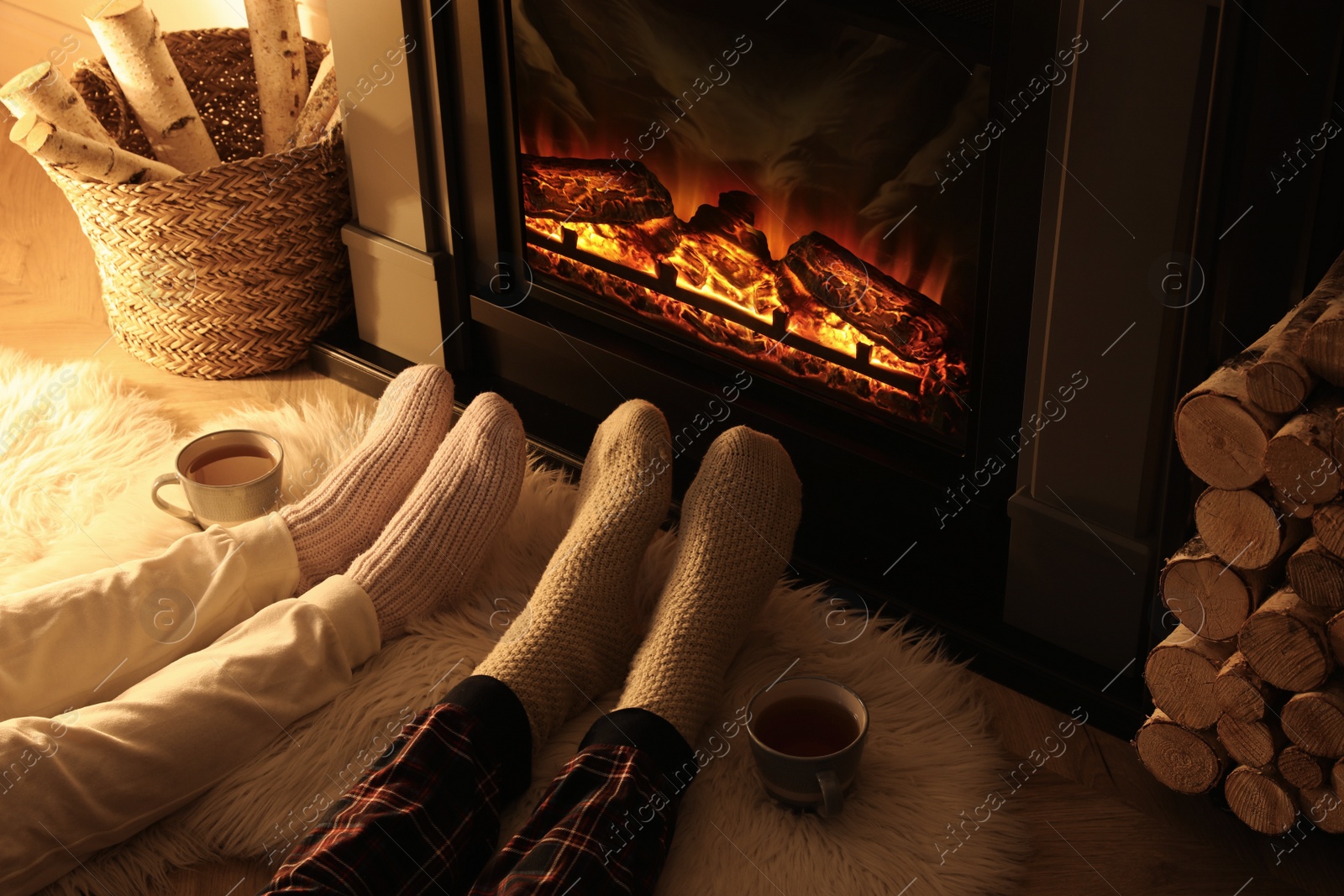 Photo of Couple in knitted socks near fireplace at home, closeup of legs