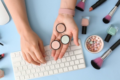 Photo of Young woman with makeup products typing on keyboard at table. Beauty blogger
