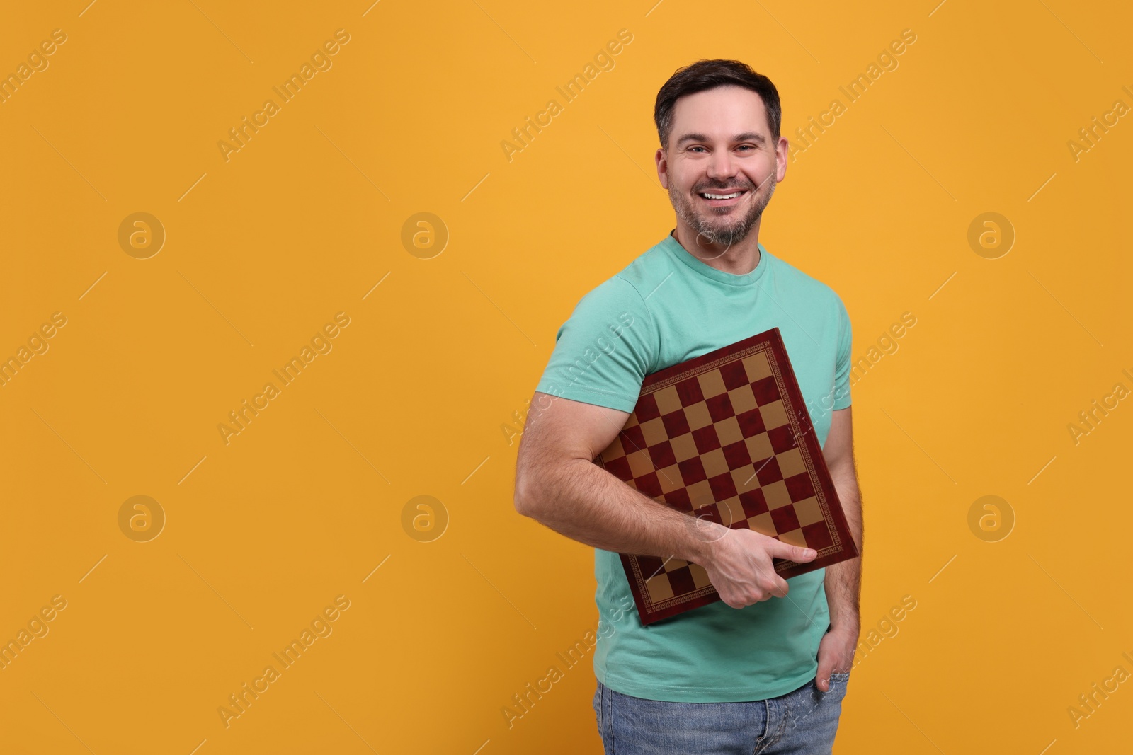 Photo of Smiling man holding chessboard on orange background, space for text