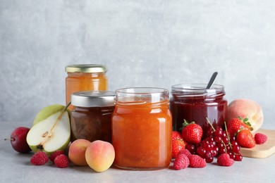 Jars with different jams and fresh fruits on grey table