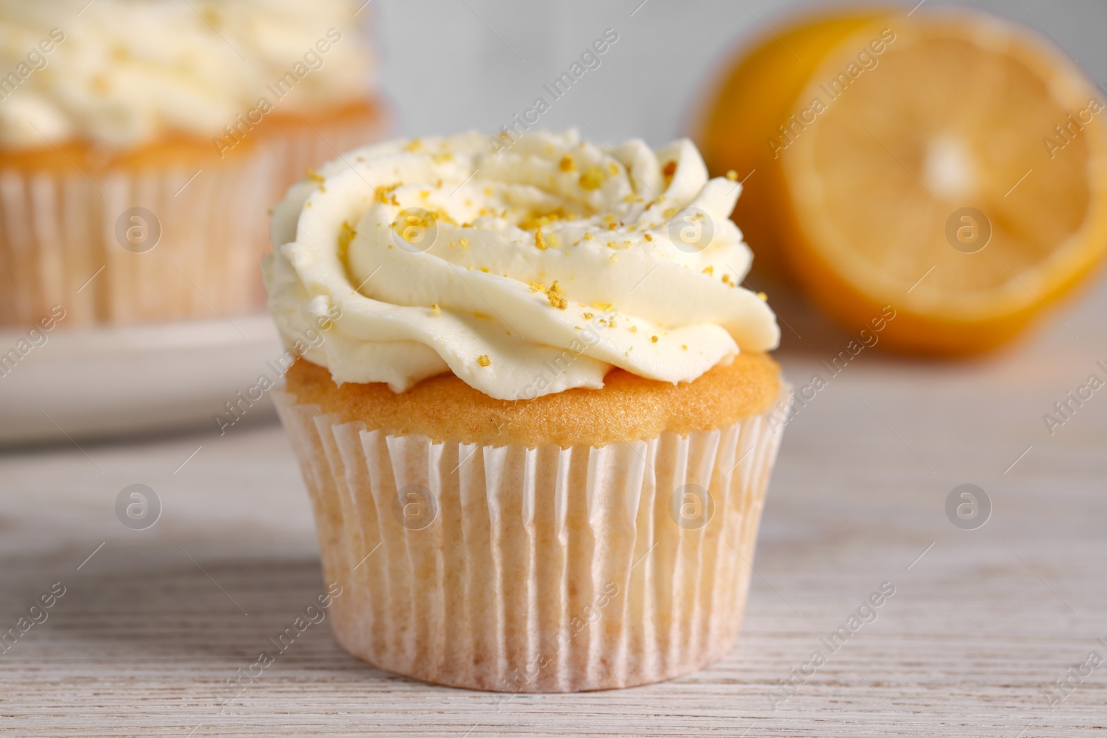 Photo of Delicious cupcake with white cream and lemon zest on light wooden table, closeup