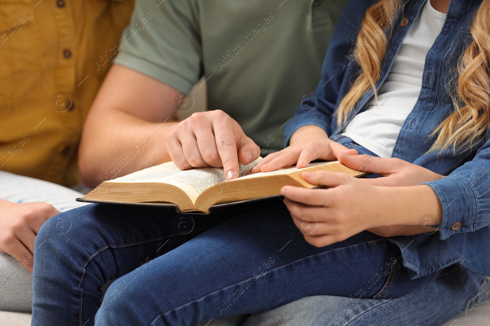 Photo of Girl and her godparents reading Bible together indoors, closeup