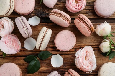 Flat lay composition with delicious macarons and roses on wooden table